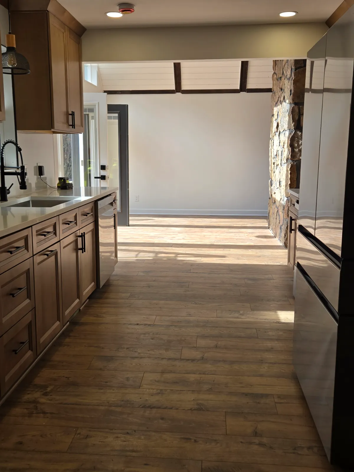 Galley kitchen with new cabinets and plank flooring opening to a sunroom
