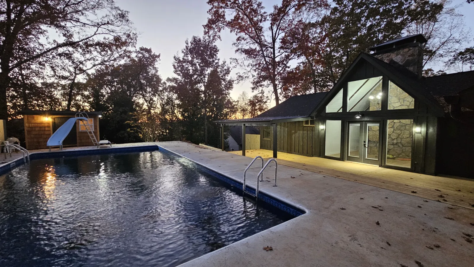 Renovated home exterior with new deck beside a pool at dusk